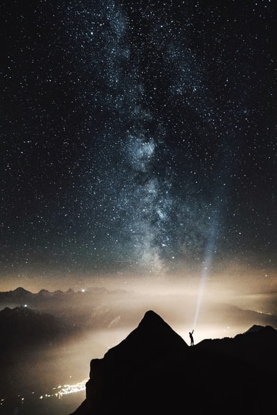 山顶上的人的剪影在夜晚用手电筒指着满天的星星